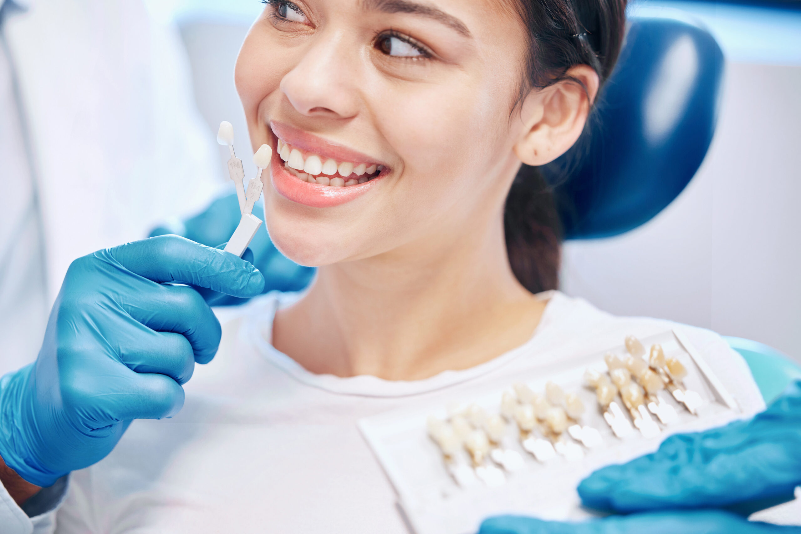 Dentist comparing tooth shades with a whitening colour guide beside a patient's smile