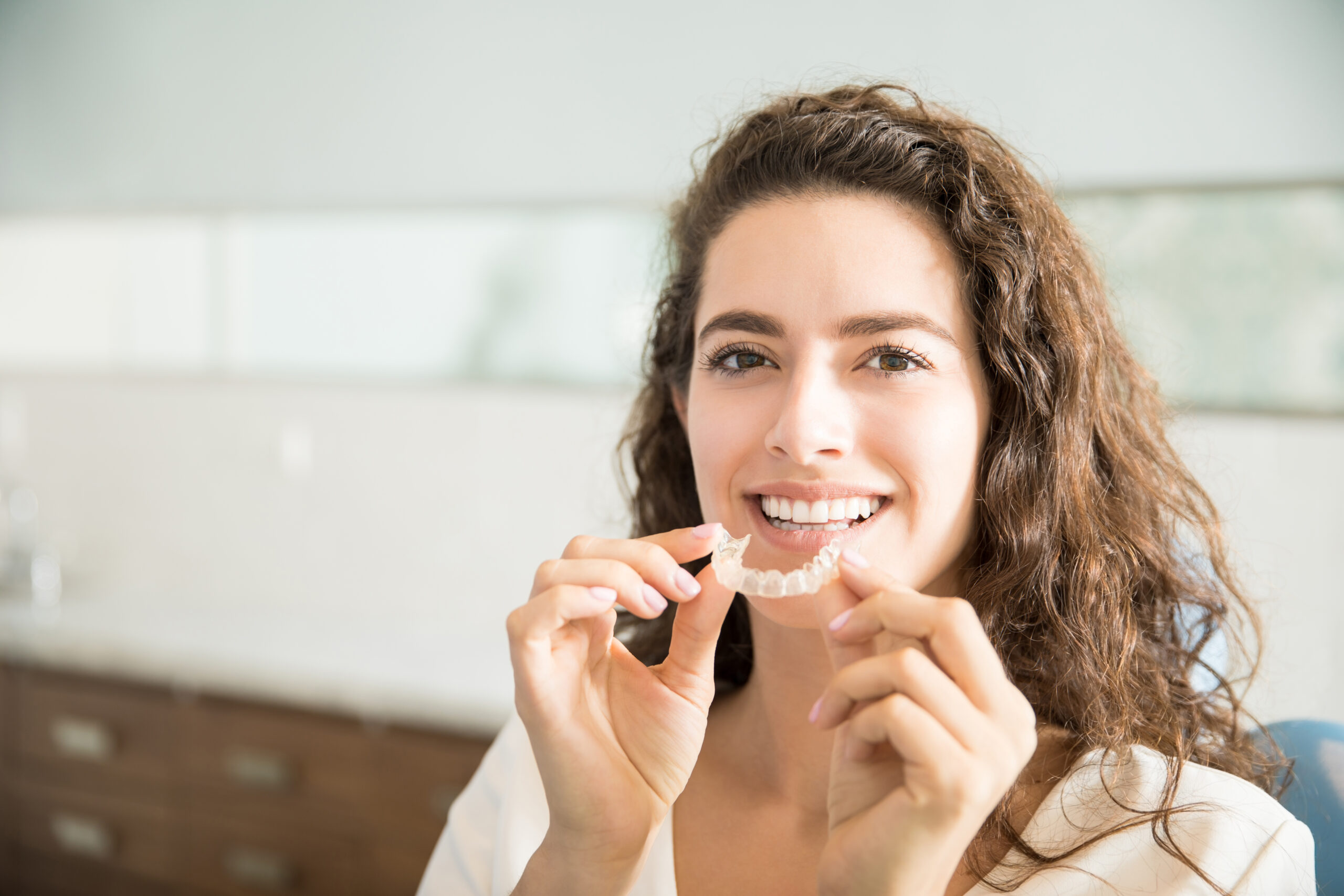 ผู้หญิงยิ้มถือเครื่องมือจัดฟันใส clear aligner ในคลินิกทันตกรรมคาซ่า สะพานควาย